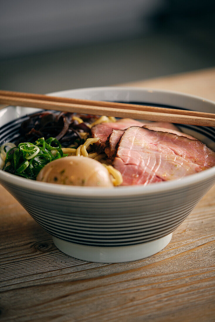 Delicious traditional ramen soup in bowl with chopsticks served on round table
