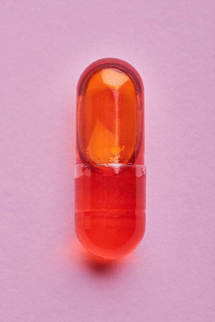 Composition of orange pills on pink background in light studio
