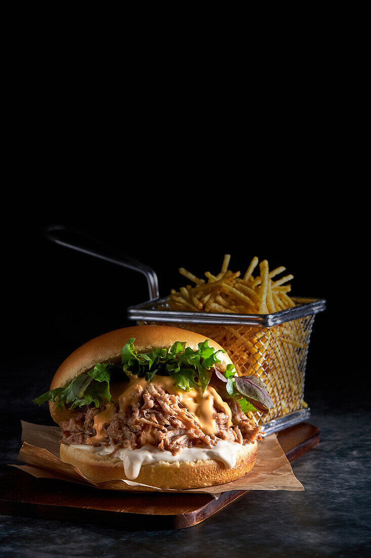 Leckerer Burger, bestehend aus Brioche-Brot mit Mayonnaise bestrichen und Schweinefleisch mit Barbecue-Sauce, Cheddar-Käse und Salatmischung, serviert mit Pommes frites