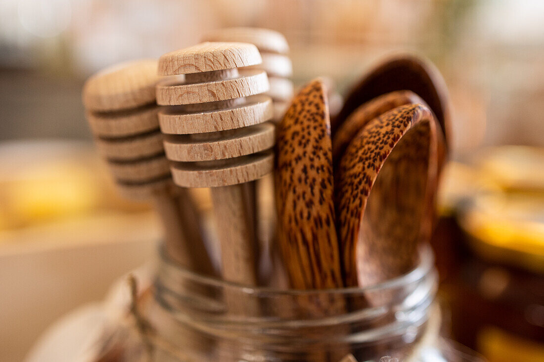 Closeup of wooden honey scoops and spoons placed in glass jar on blurred background
