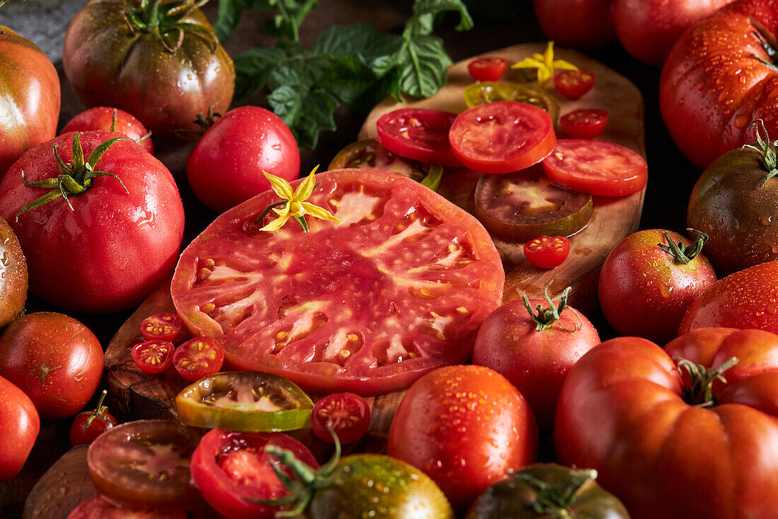 High angle of sliced tomato among ripe whole red tomatoes with water drops