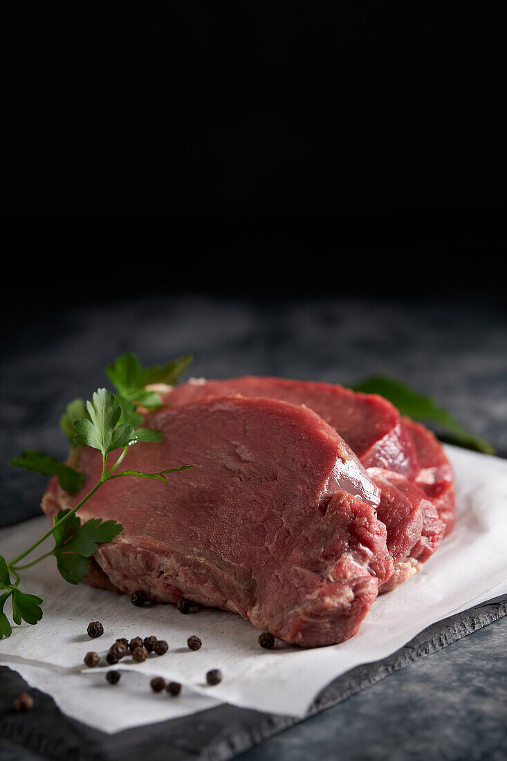 Von oben frisches, ungekochtes Rinderfilet mit grüner Petersilie auf einer Schiefertafel mit Pergamentpapier in der Küche