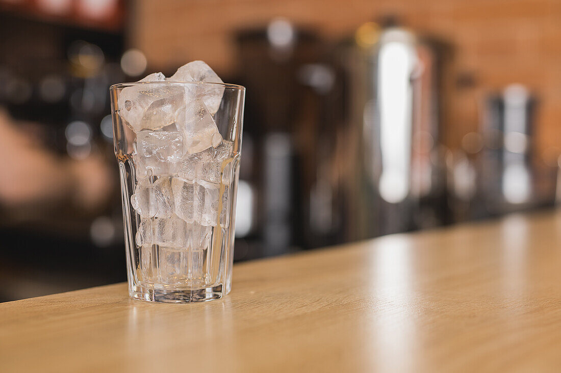 Transparentes Glas mit Eiswürfeln für ein Erfrischungsgetränk auf einer hölzernen Arbeitsplatte in einer Bar