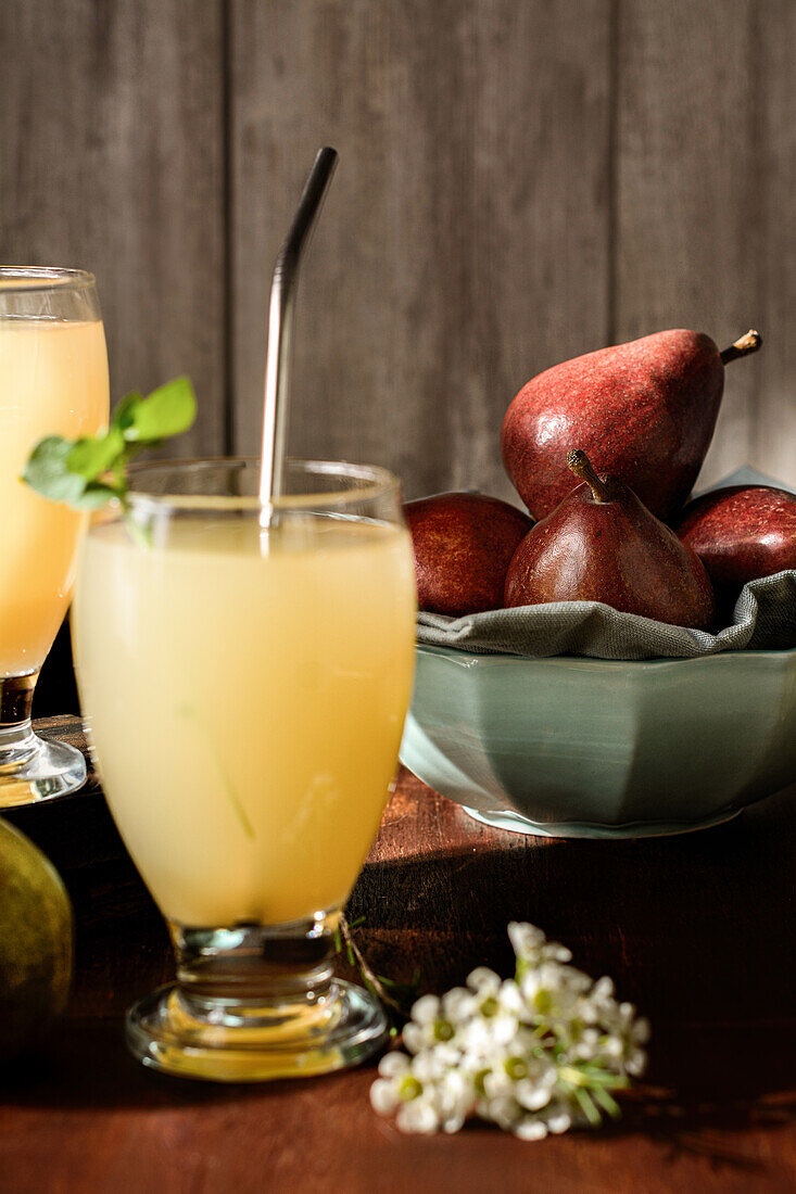 Glasses of delicious refreshing drinks with pear juice and fresh elderflower leaves on table