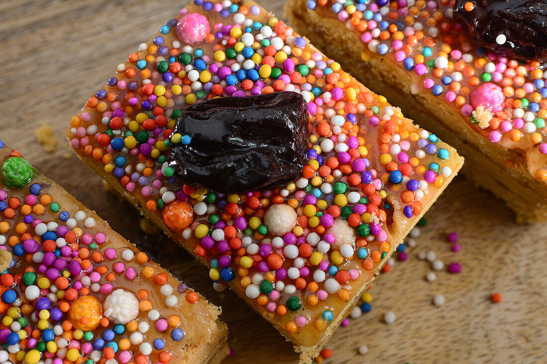 Ansicht von oben von süßen Turron de Dona Pepa-Kuchen mit Nougat, dekoriert mit bunten Dragees und Pflaumen, serviert auf einem Holztisch