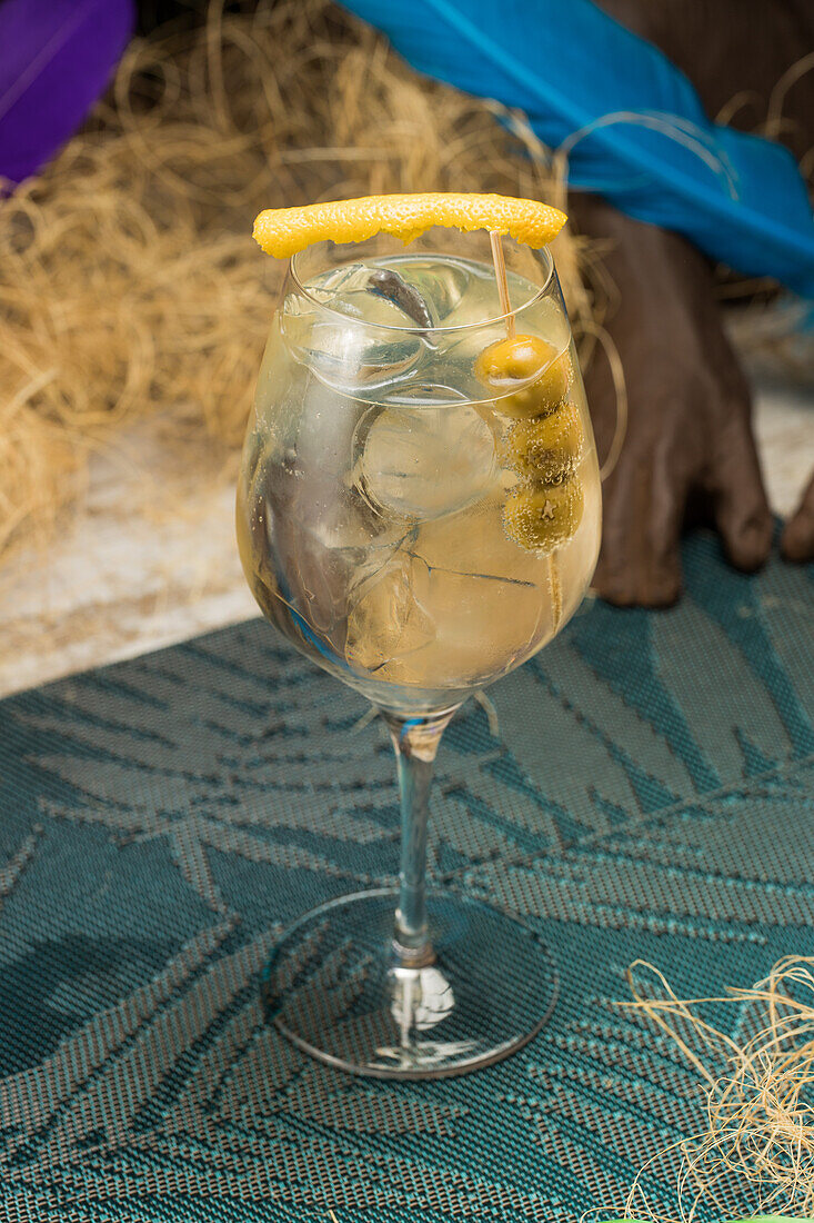 Crystal wineglass with Martini cocktail served with lemon zest and olives edge placed against dry grass