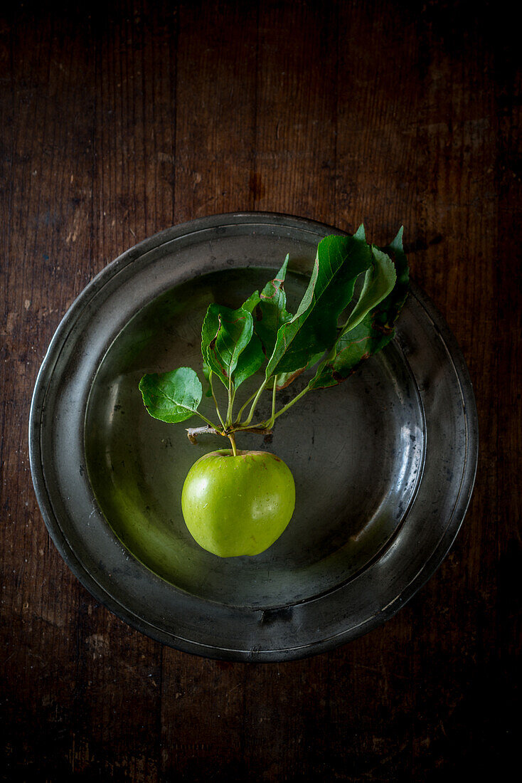 From above ripe green apple with foliage on plate on wooden table background
