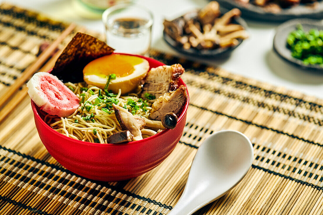 Von oben auf appetitliche Ramen-Suppe mit Fleisch und Ei und Nudeln, serviert in einer Schüssel auf einem Tisch neben Stäbchen und einer Glastasse