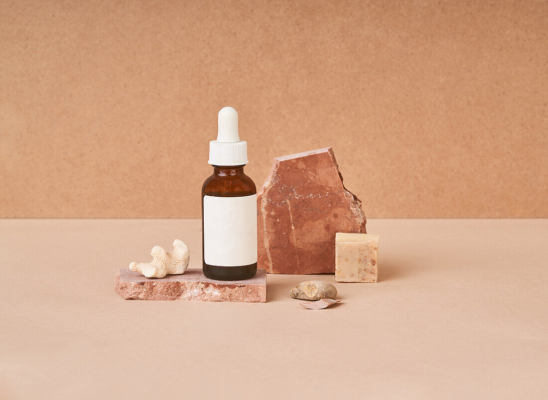 Small bottle of beauty oil and natural handmade soap pieces with pumice stone on two color background