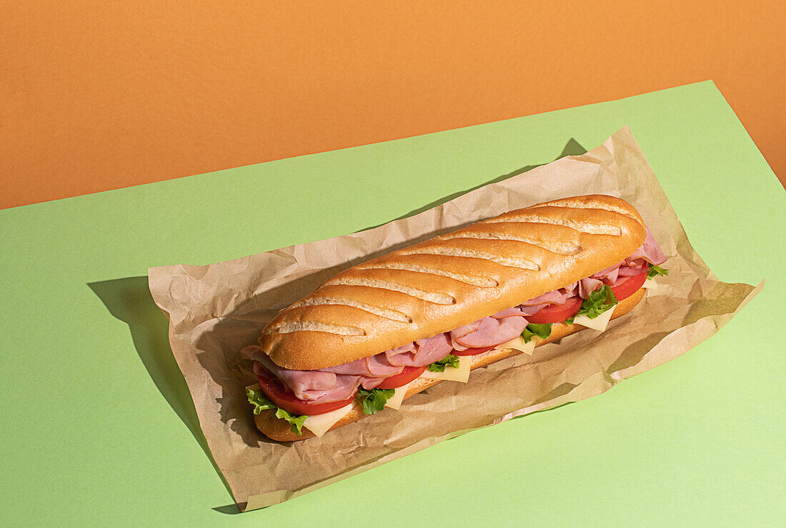 From above appetizing sandwich with ham and fresh lettuce served on baking paper on colorful table background