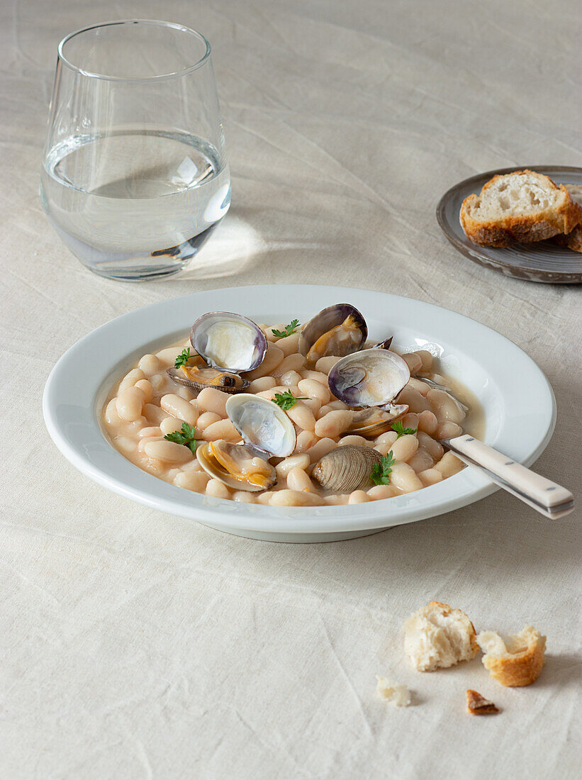Appetitanregender traditioneller spanischer Bohneneintopf mit Mollusken in einem Teller mit frischen Petersilienblättern auf einem Tischtuch