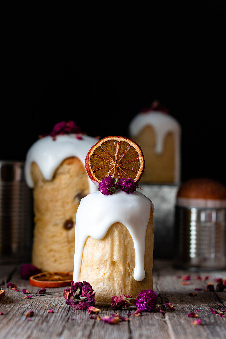 Several delicious homemade kulichs poured with sweet glaze and decorated with pieces of dry orange and flowers on wooden table