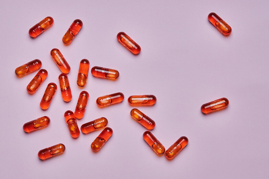 Top view composition of orange pills scattered on pink background in light studio