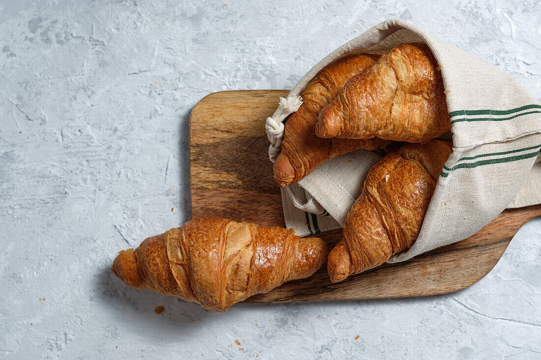 Freshly baked croissants served on wooden cutting board with napkin on table for breakfast