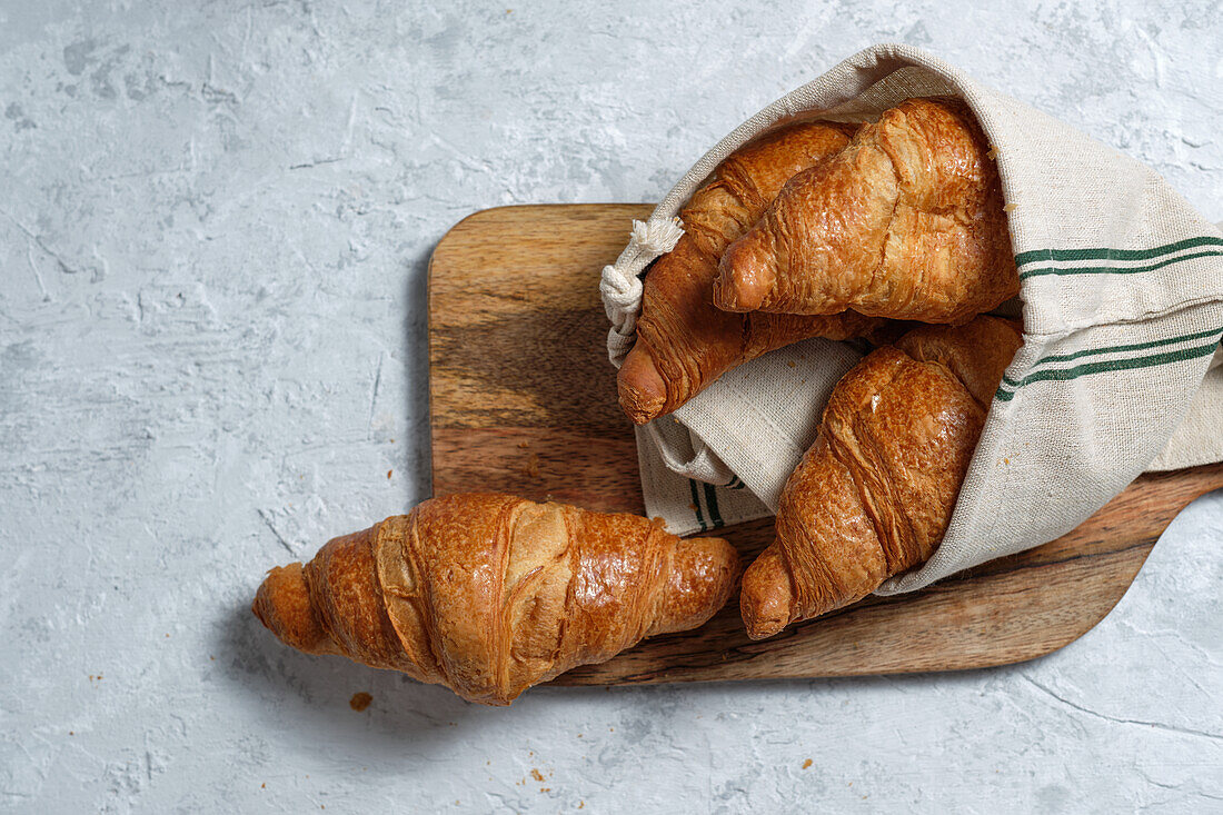 Frisch gebackene Croissants, serviert auf einem Holzbrett mit Serviette auf dem Frühstückstisch