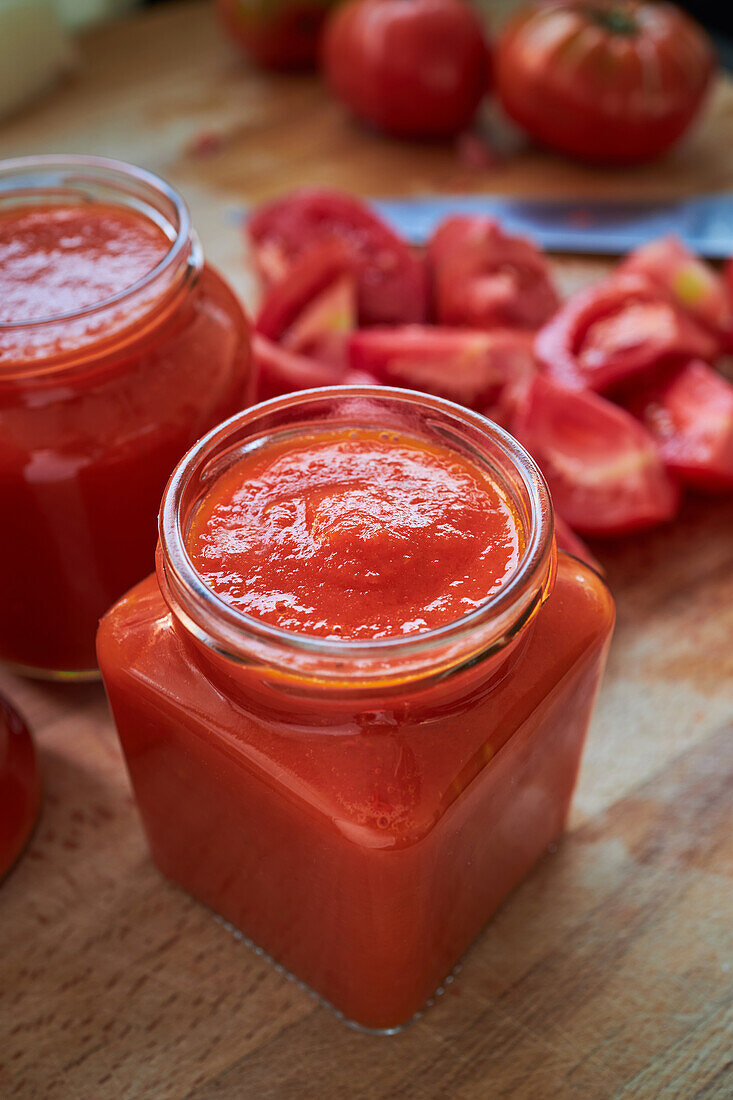 Von oben reife rote Tomaten und Gläser mit Soße auf dem Tisch in der Küche