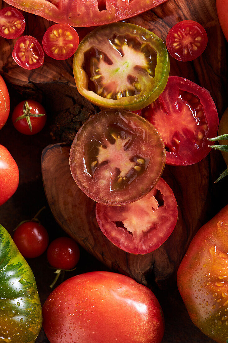 High angle of sliced tomato among ripe whole red tomatoes with water drops