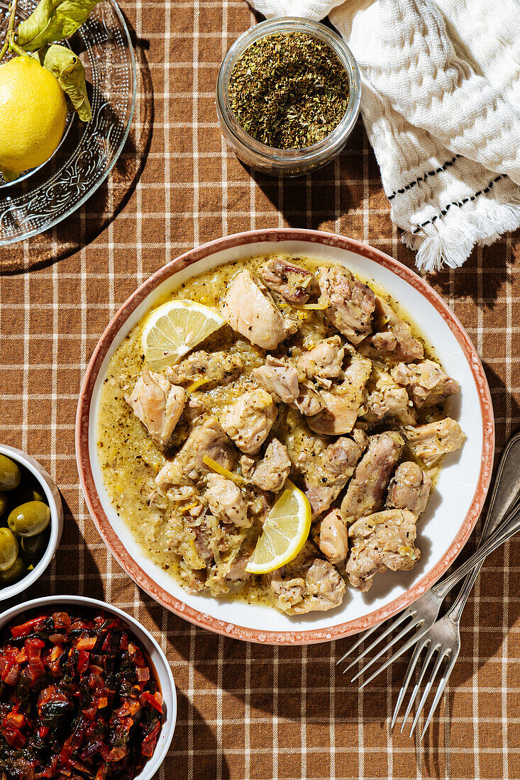 Draufsicht auf traditionellen griechischen Rindfleischeintopf mit Zitrone, serviert auf einem Tisch mit Oliven und Gewürzen in einer hellen Küche
