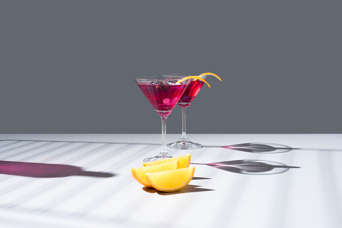 Composition of glass filled with red fruit cocktail near orange slides and zest placed on concrete table against grey background