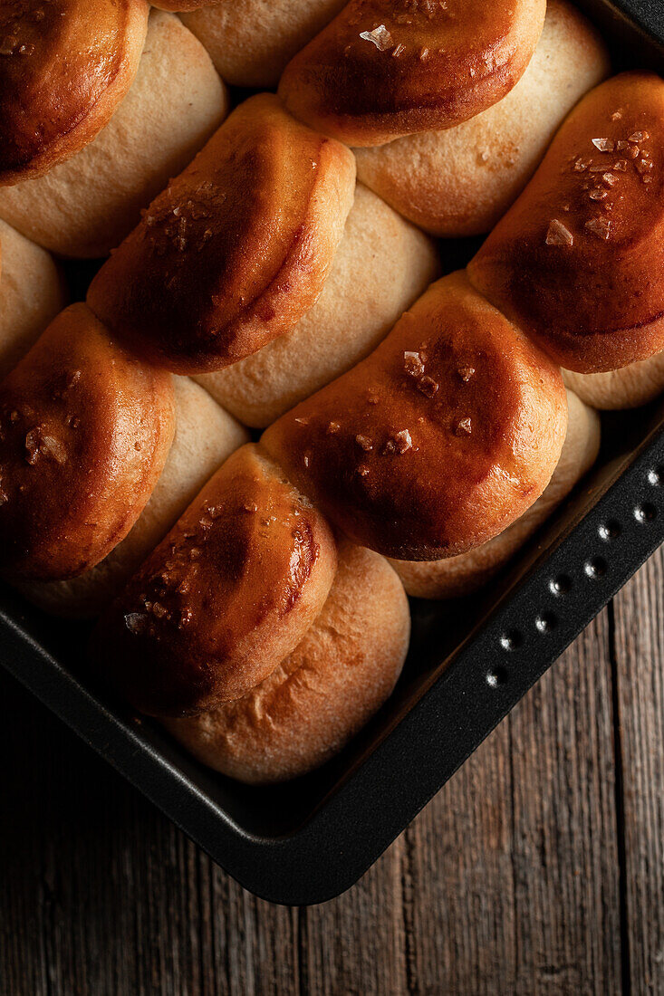 Top view of baked tasty soft dinner rolls on tray placed on wooden surface in dim light