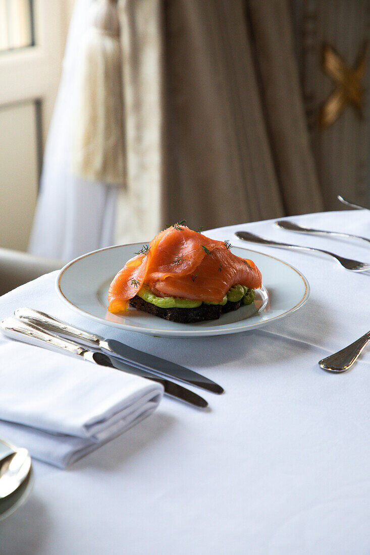 High angle of plate with delicious avocado toast with poached egg and smoked salmon served on table with cutlery and coffee cup during breakfast in hotel restaurant