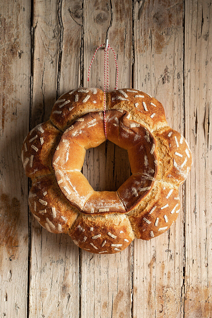 Baked round decorative bread with white patterns hanging on red thread on wooden wall with metal hook in light kitchen