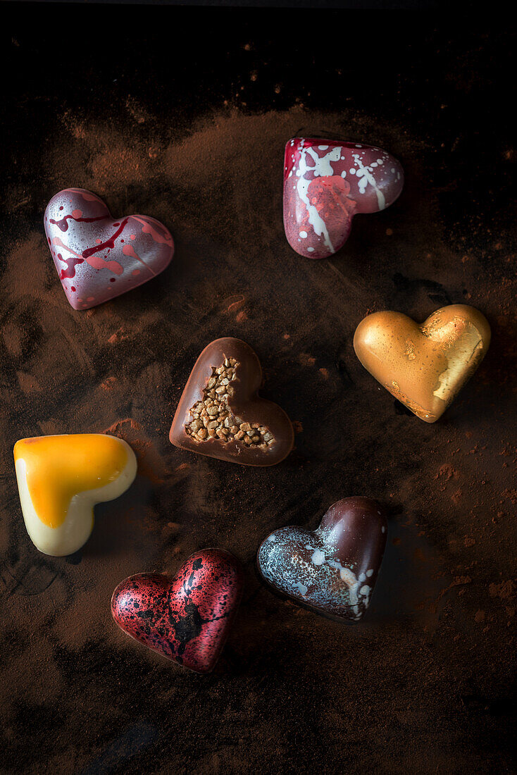 Top view composition with handmade multicolored chocolate bonbons in shape of heart on wooden table