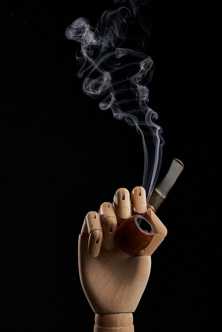 Traditionelle Tabakspfeife mit Rauch in einer hölzernen Hand auf schwarzem Hintergrund in einem Studio