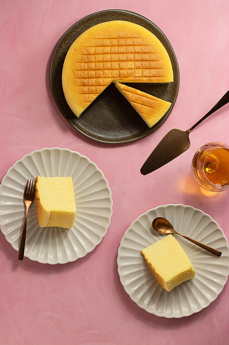 Top view of delicious cotton cheesecake served on plates near glass and spatula on pink background