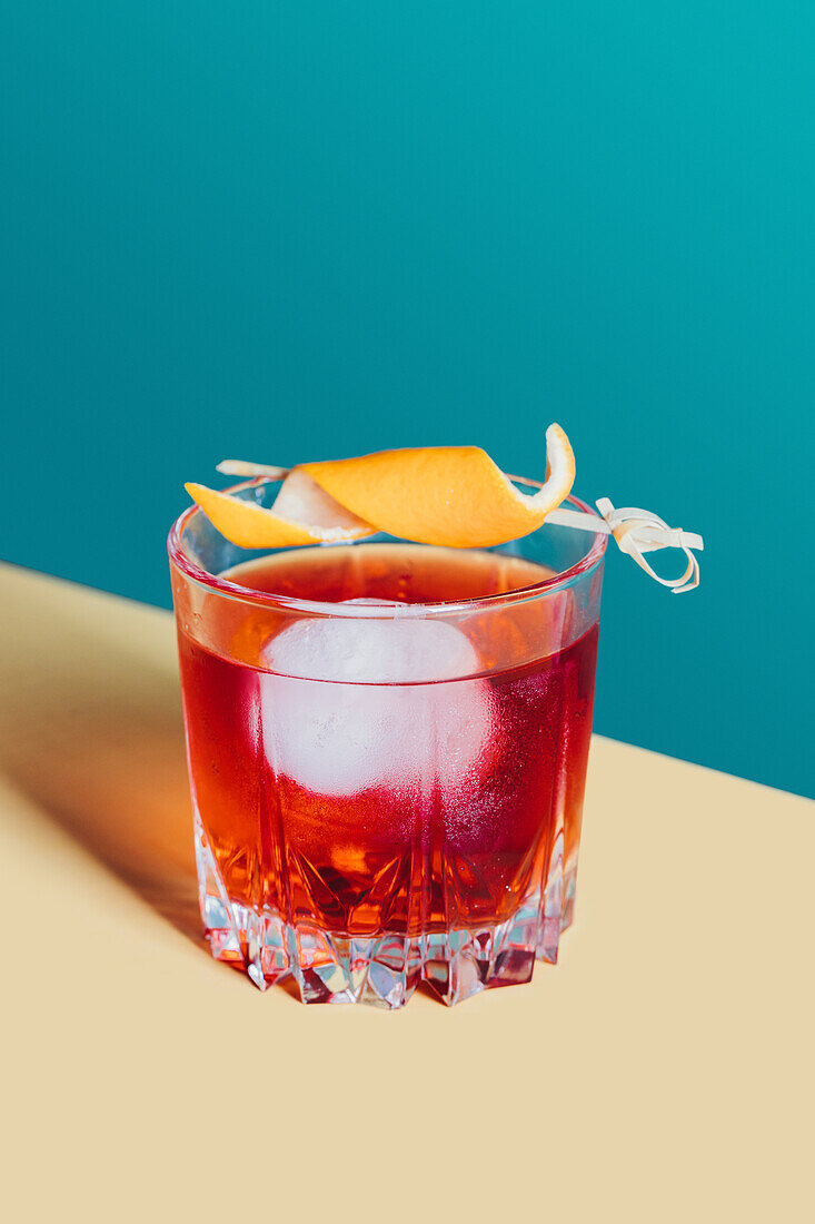 Glass of bitter alcoholic Negroni cocktail served with ice and orange peel on light surface