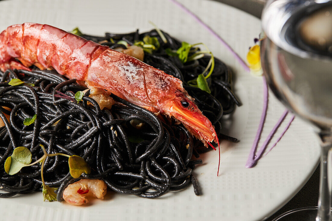 Schwarze Spaghetti mit Tintenfischtinte, garniert mit Garnelen und Sprossen, serviert auf einem Teller während des Mittagessens im Restaurant