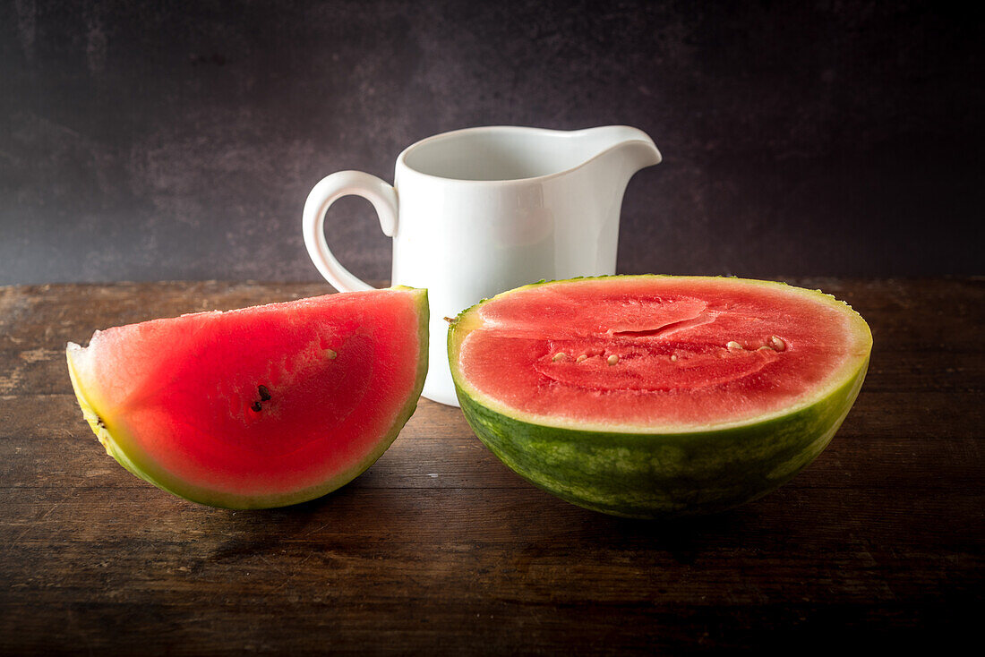 Slices of ripe sweet watermelon placed on wooden table on dark background near ceramic jug