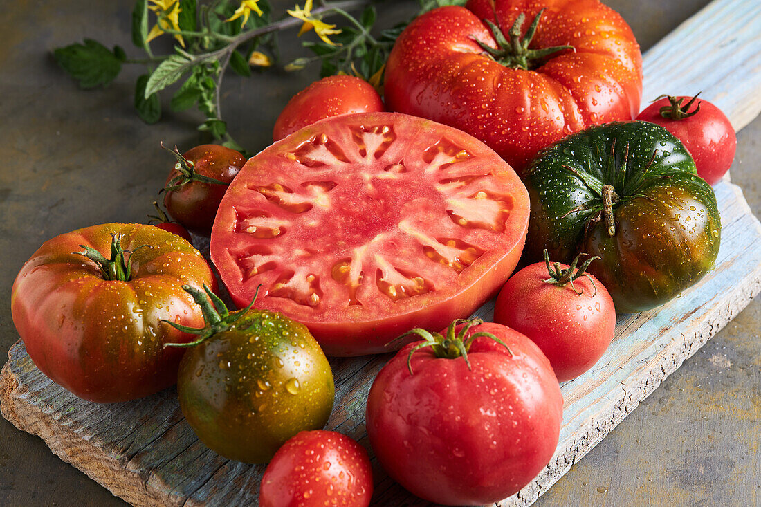 High angle of sliced tomato with salt placed on wooden chopping board among ripe red tomatoes with water drops