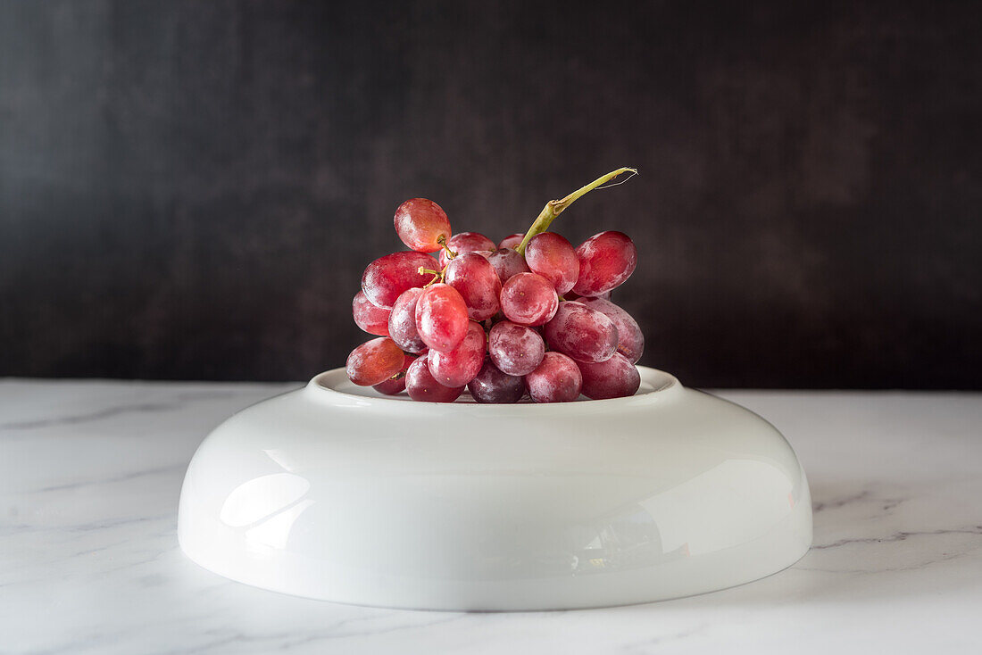 Bunch of sweet pink grape served on plate on white background