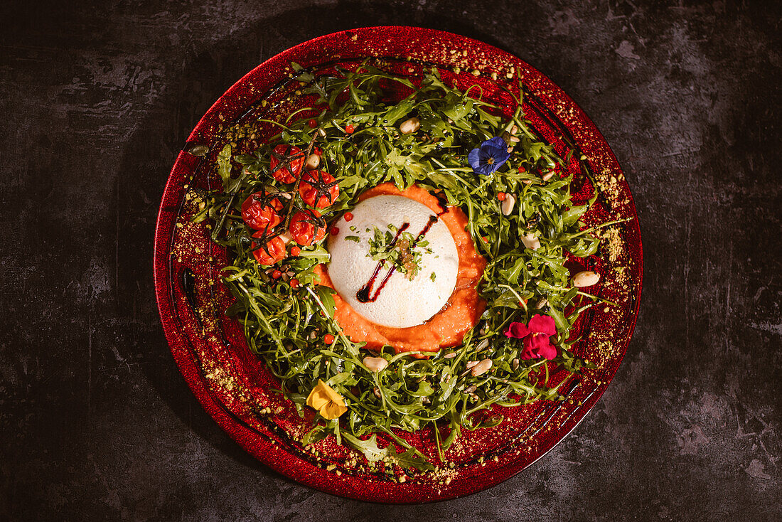 Blick von oben auf leckeren Burrata-Käse auf kalter Tomatencreme mit Rucolablättern und Kirschtomaten mit Trüffeln und Erdnüssen