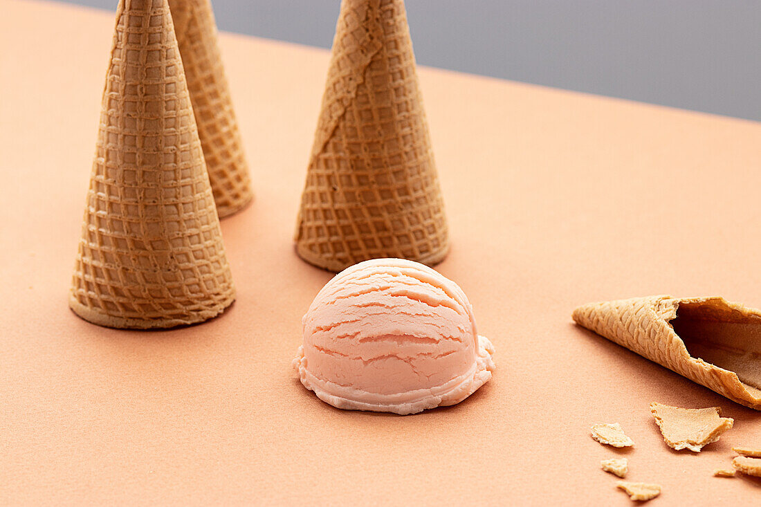 Pink ice cream scoop and waffle cones placed on table in studio