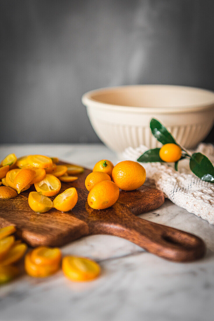 Pile of fresh orange cut kumquats on wooden chopping board placed on marble table with towel in kitchen