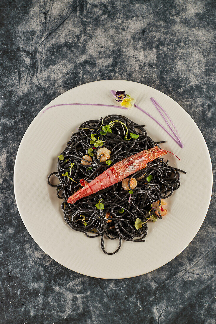 Von oben schwarze Spaghetti mit Tintenfischtinte, garniert mit Garnelen und Sprossen und serviert auf einem Teller während des Mittagessens im Restaurant