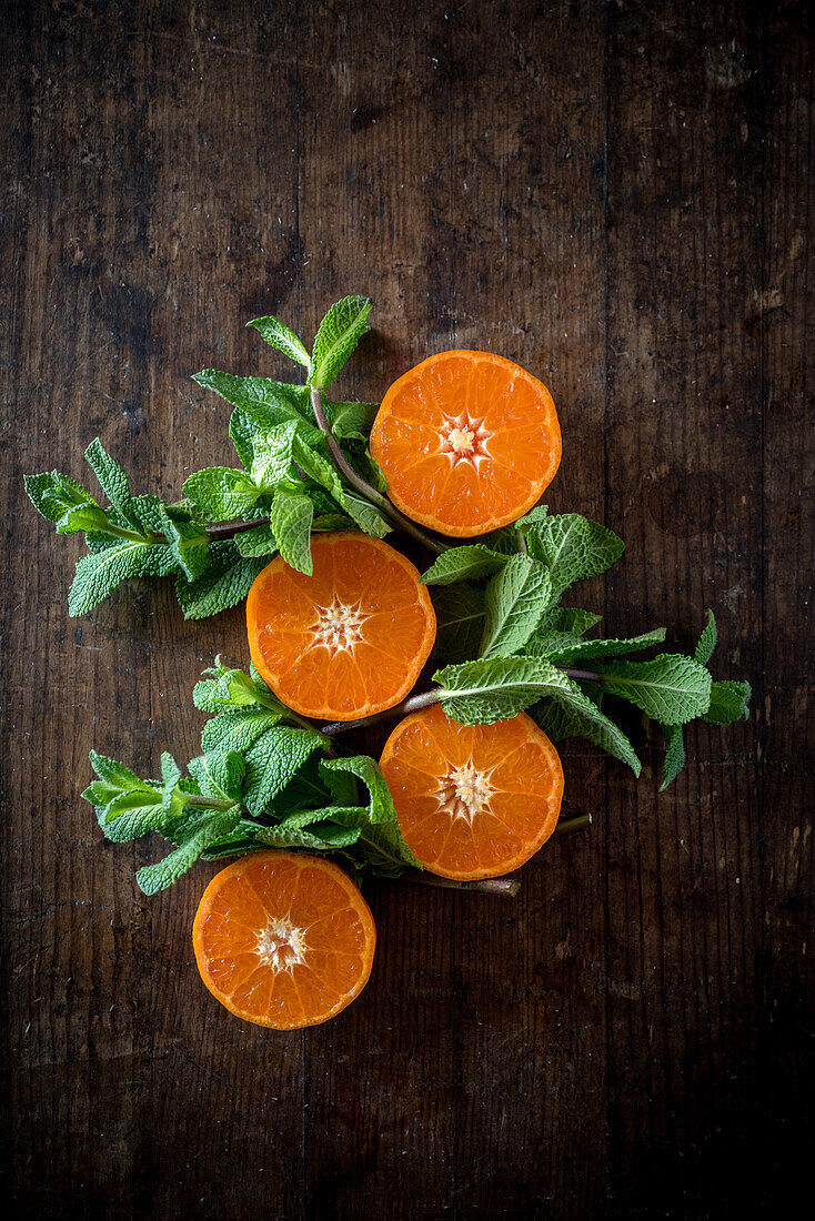 Overhead view of fresh tangerine halves with juicy pulp among mint foliage on brown background