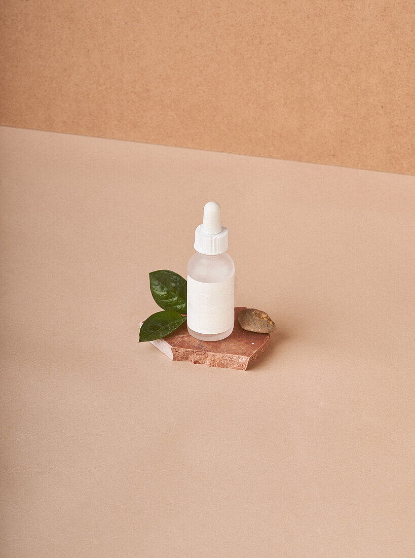 Kleine weiße Flasche mit kosmetischem Serum auf gestapelten braunen Marmorsteinen auf Stoff vor beigem Hintergrund