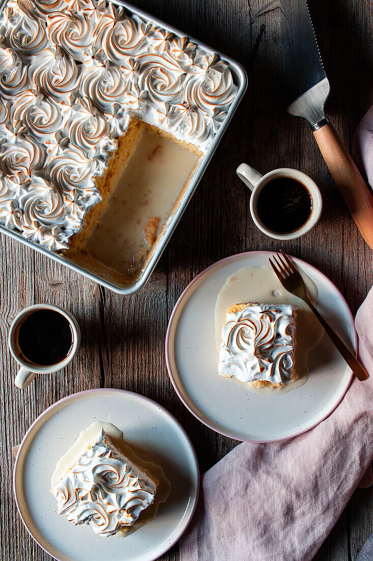 From above three milks cake in baking dish and plates with cups of strong coffee on wooden table
