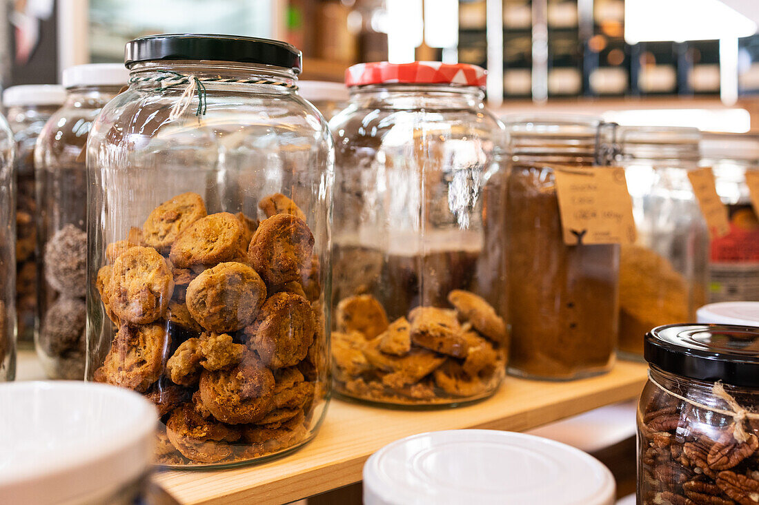 Verschiedene Arten von Keksen und getrockneten Früchten und Gewürzen in Glasgefäßen auf Holzregalen in einem lokalen Geschäft