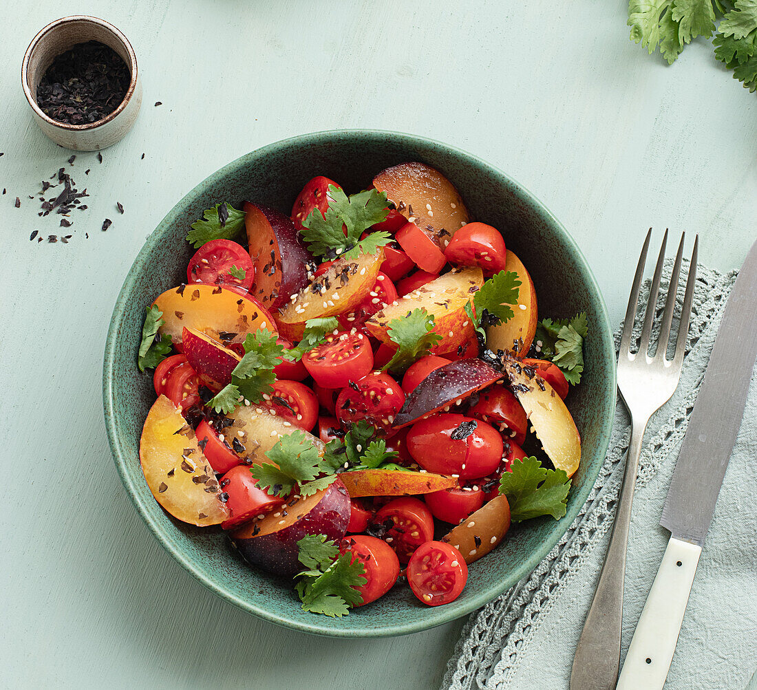 Top view of a raw tomato salad with fruit on a table with green tablecloth surrounded by healthy ingredients