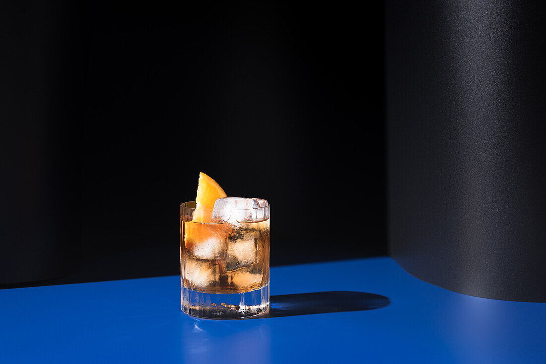 Glas alkoholischer Cocktail mit rotem Wermut, serviert mit Orangenscheiben in einem hellen Studio mit blauer und schwarzer Wand