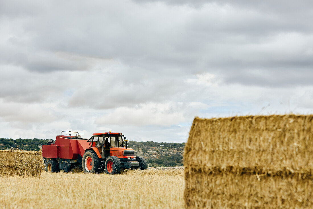 Dried hay roll and modern tractor placed on agricultural field in mountainous area in summer