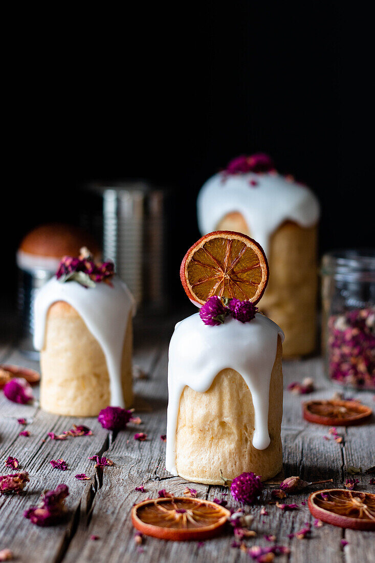 Several delicious homemade kulichs poured with sweet glaze and decorated with pieces of dry orange and flowers on wooden table