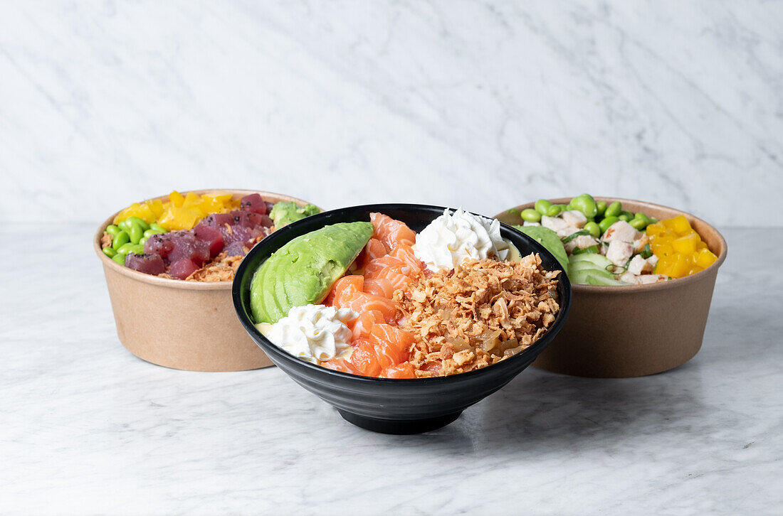 Bowls with delicious poke dish with assorted ingredients placed on marble table in kitchen