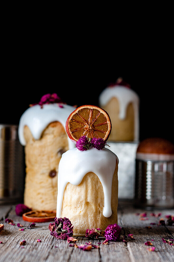 Several delicious homemade kulichs poured with sweet glaze and decorated with pieces of dry orange and flowers on wooden table