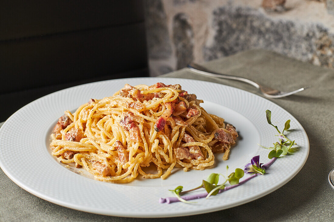 Leckere Spaghetti Carbonara mit Speck und Parmesan, gemischt mit Ei, serviert auf einem Teller mit Sprossen und Blumen beim Mittagessen in einem italienischen Restaurant
