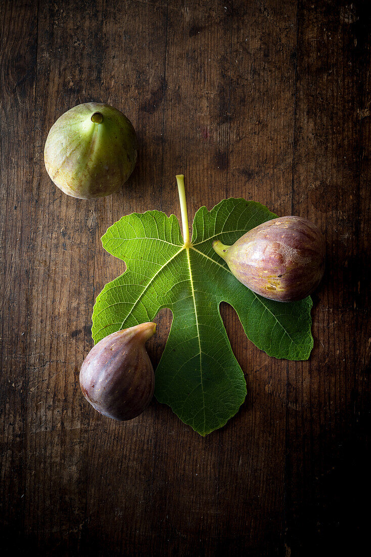 Top view of ripe halved and whole figs placed with green leaf on wooden rustic table